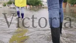 girls in raincoats and rubber boots walk along road flooded with torrential rains, their feet walk