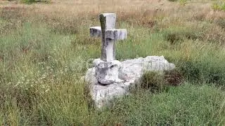 Stone cross as a tombstone of an old tomb in a grassy field. A single grave surrounded by grass....