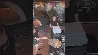 Two pizza restaurant employees have trouble picking up the pizza and getting it into the o
