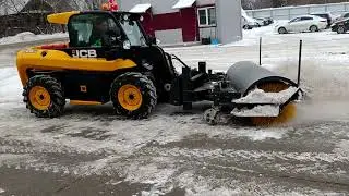 Cleaning of the territory from snow and ice with a brush on a JCB mini loader